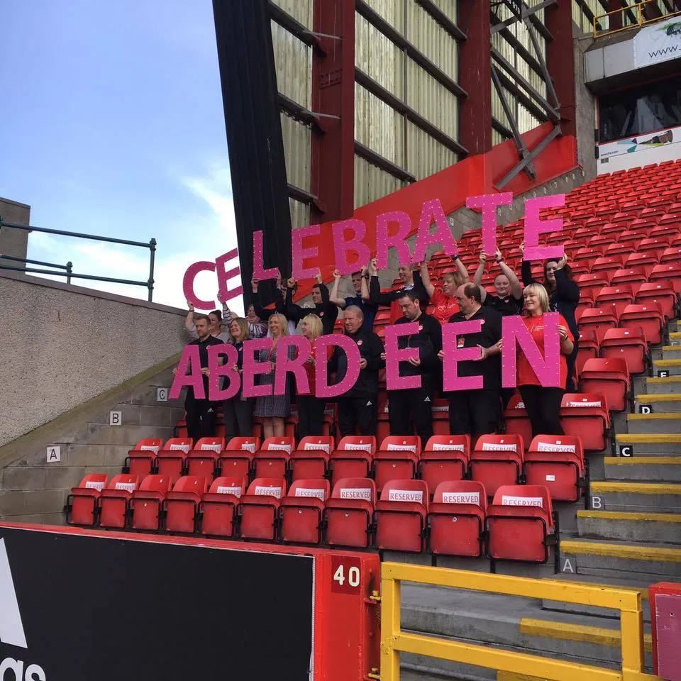 Celebrate Aberdeen volunteers holding giant pink letters at Pittodrie